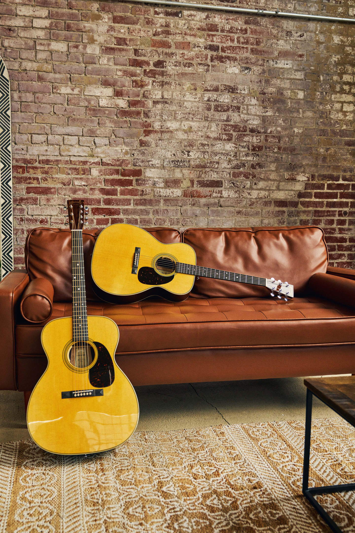 Johnny Marr signature guitars on a brown leather couch against a brick wall