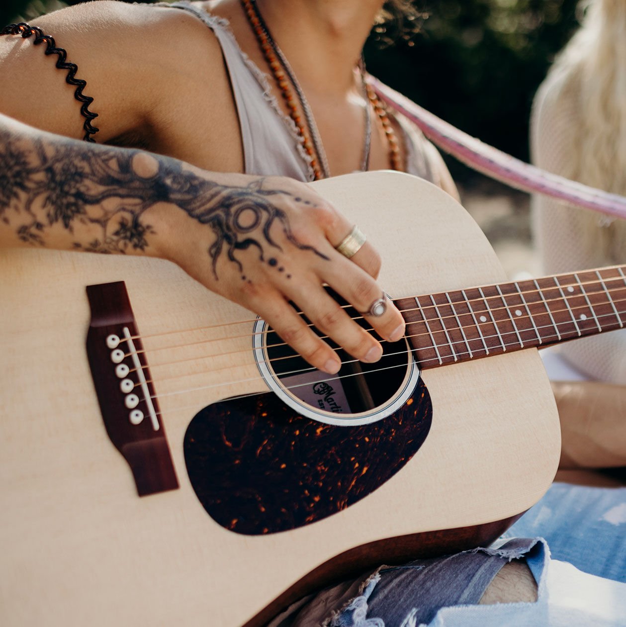 Person with tattoos playing an acoustic guitar