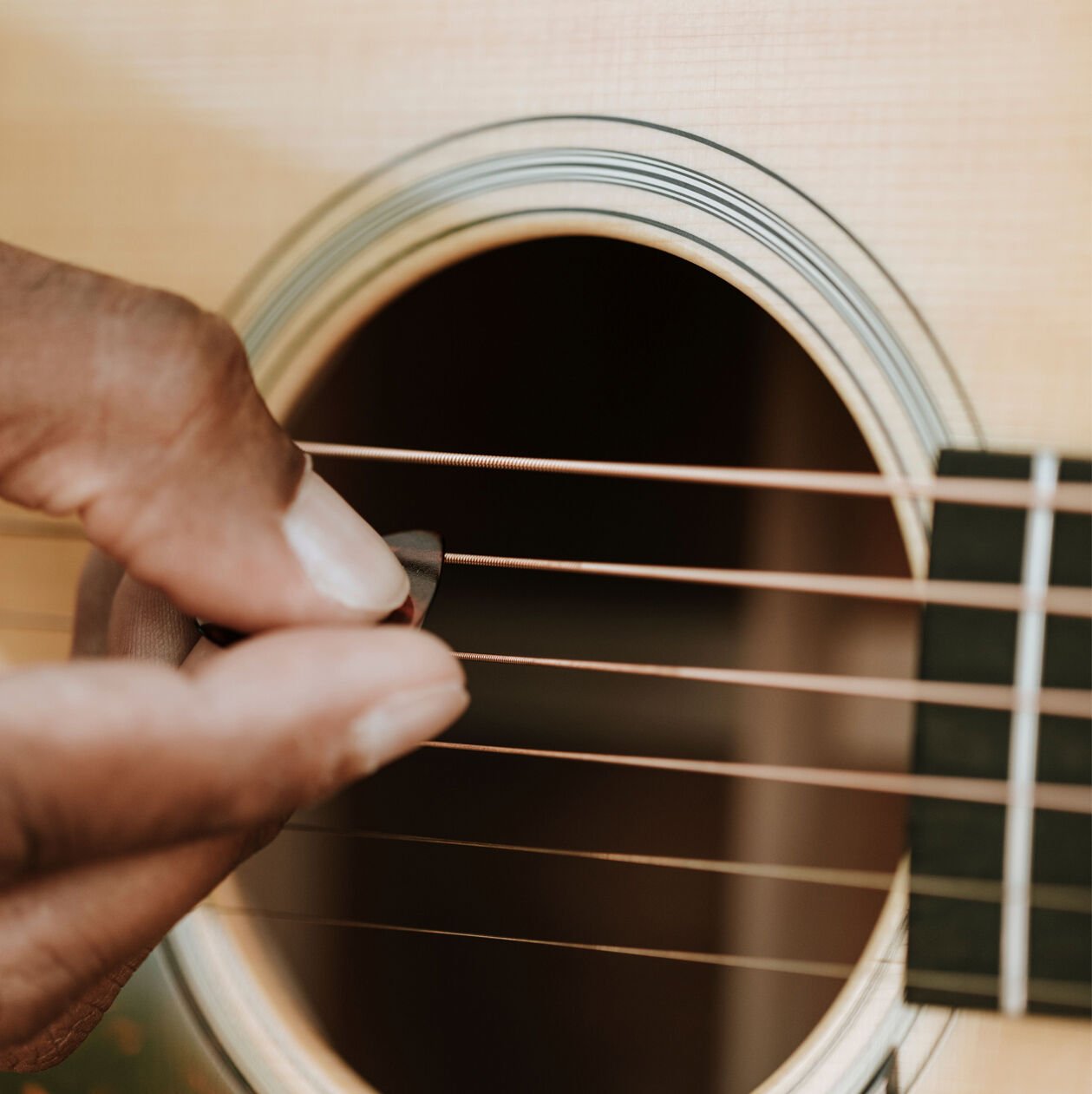 Closeup of a person strumming acoustic guitar strings with a pick