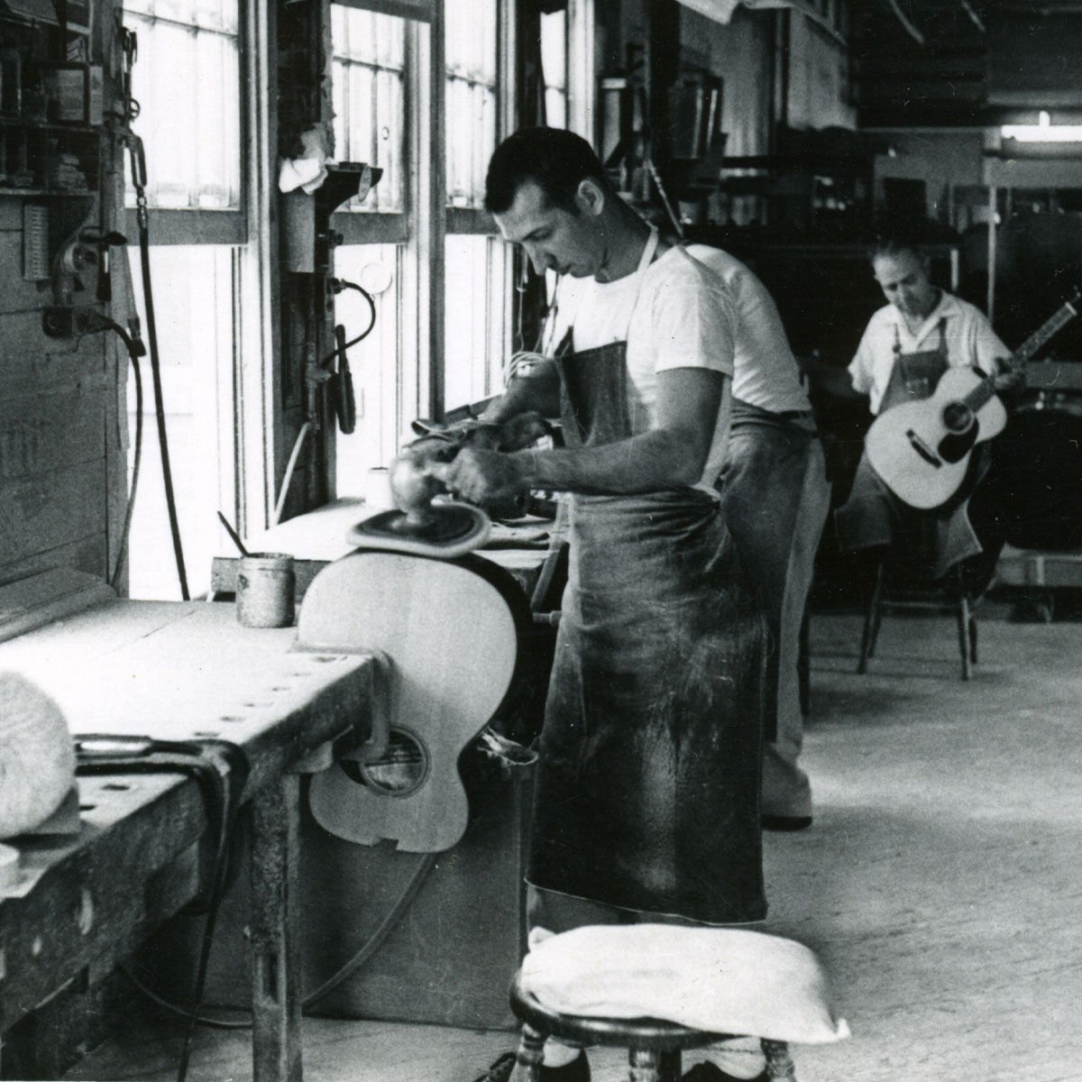 Black and white photo of a worker polishing a guitar