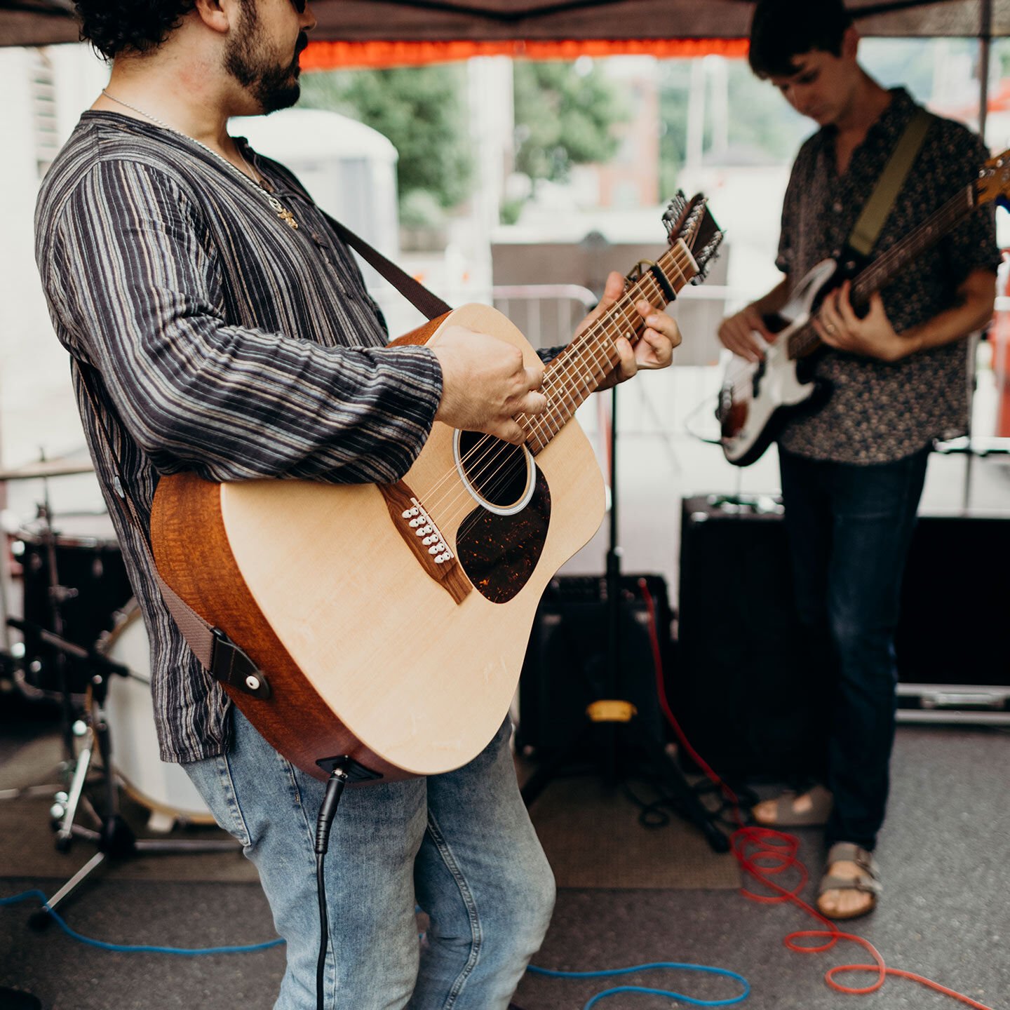 Two people playing guitar at a street fair Two people playing guitar at a street fair