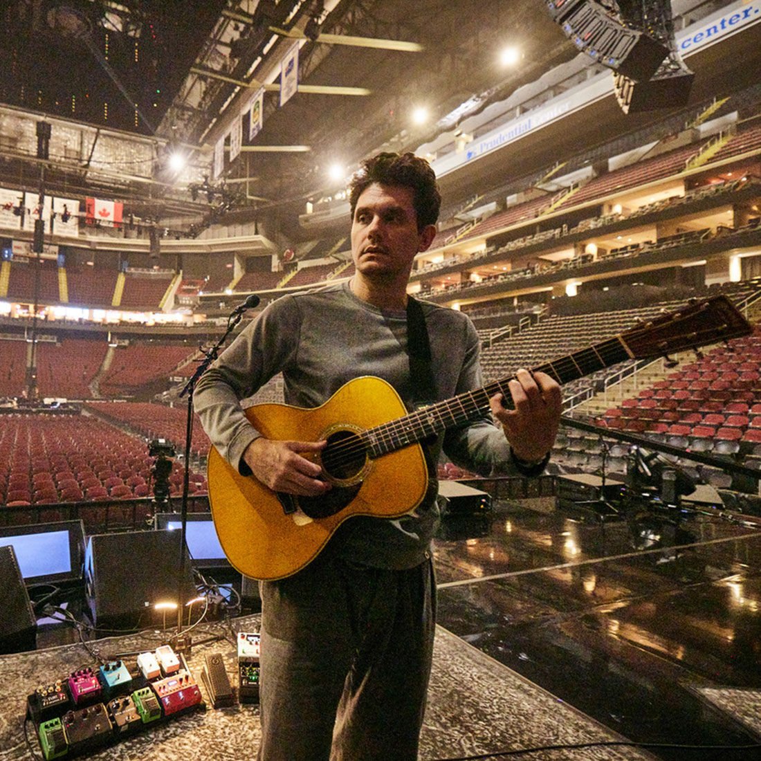 John Mayer holding guitar in an empty stadium