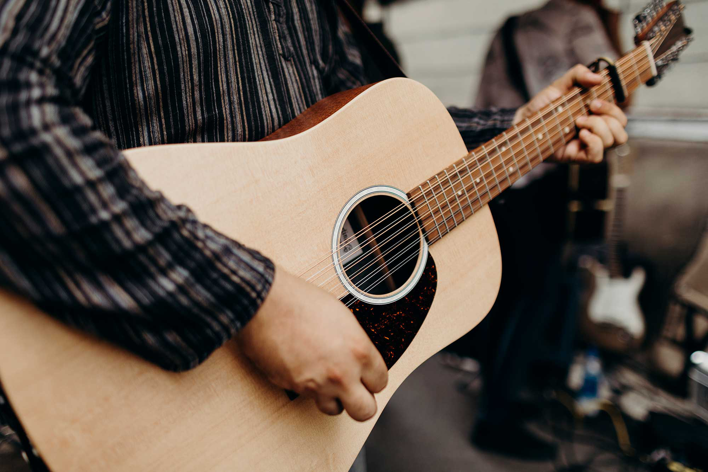 Person in a flannel shirt strumming an acoustic guitar with a capo on the third fret