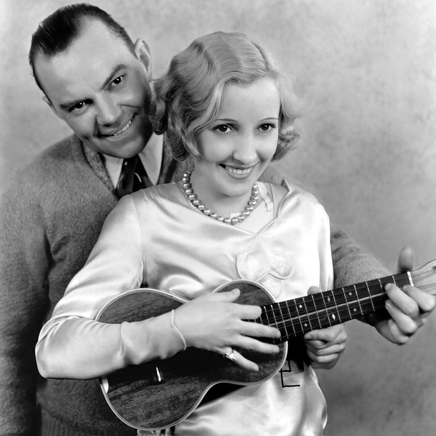 Black and white photo of a man standing behind a woman playing a ukulele