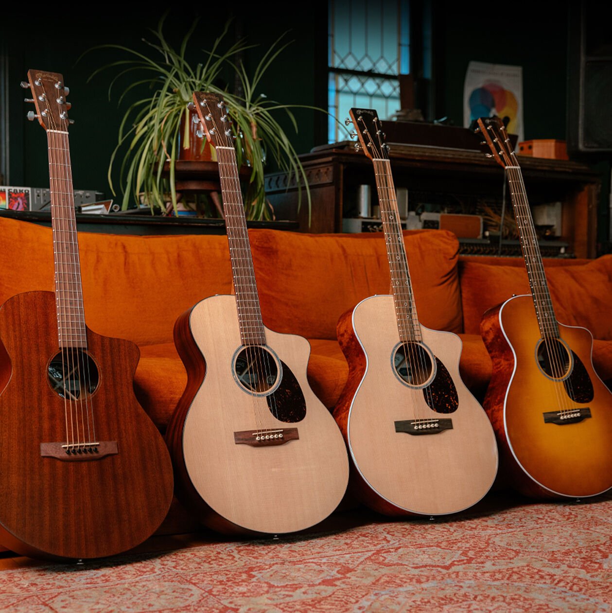 Four SC model acoustic guitars lined up leaning against a sofa