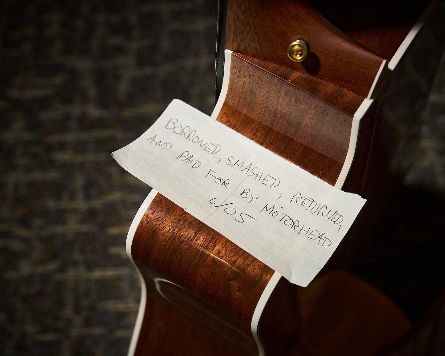 A note on an acoustic guitar that reads "Borrowed, smashed, returned, and paid for by Motorhead 6/05"