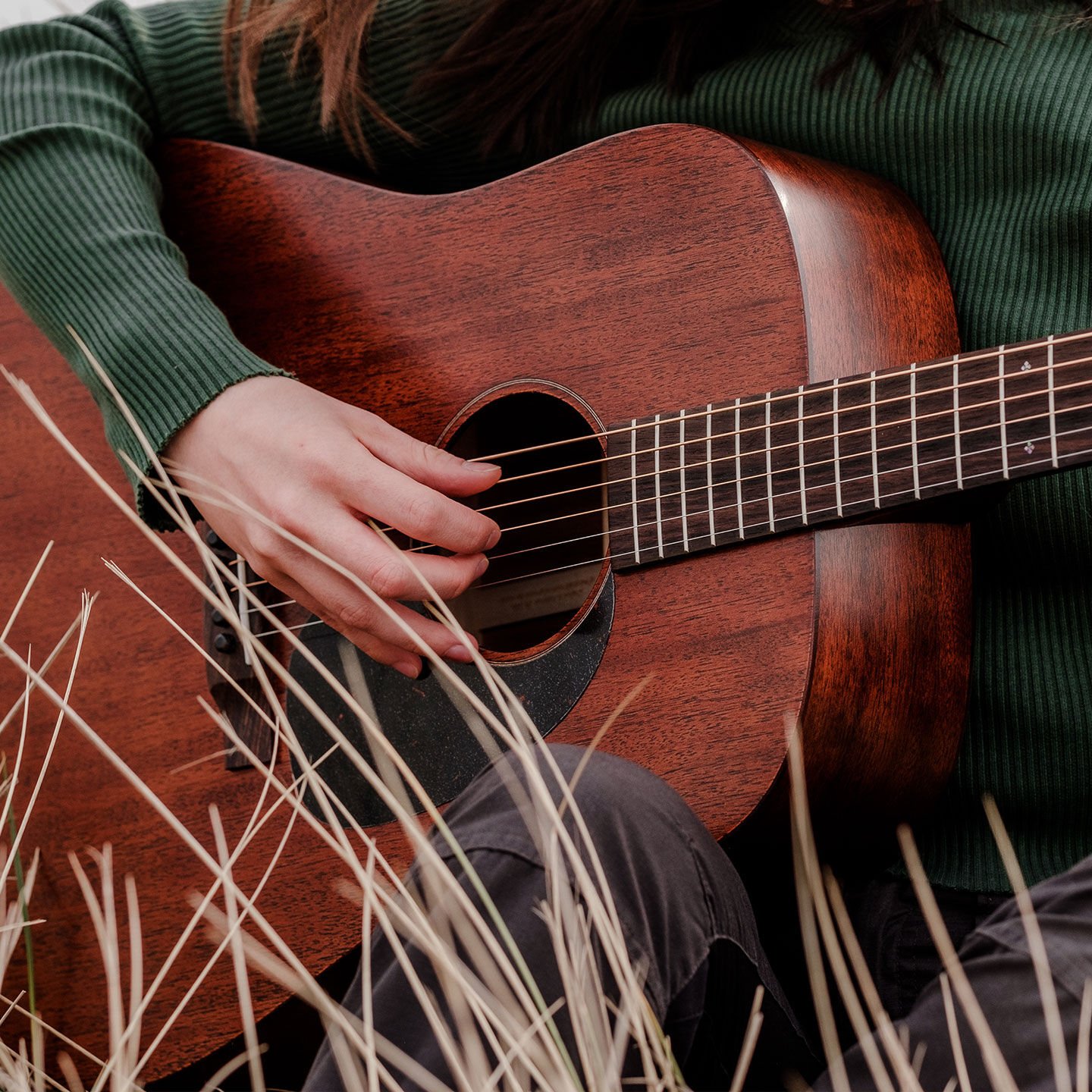 Close up of person playing guitar seated in tall grass