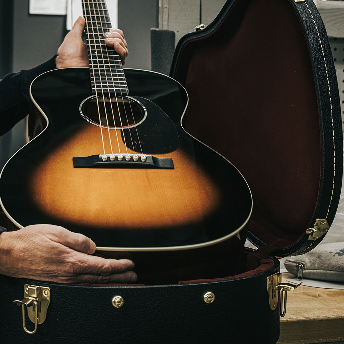 Person placing a sunburst acoustic guitar into a case