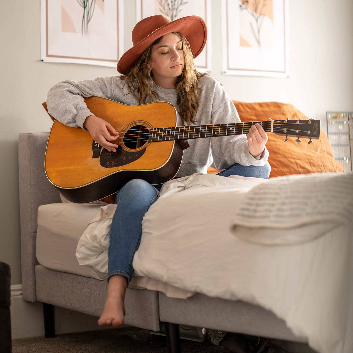 Young woman in a red brimmed hat sitting on a bed playing a Martin dreadnought. Young woman in a red brimmed hat sitting on a bed playing a Martin dreadnought.