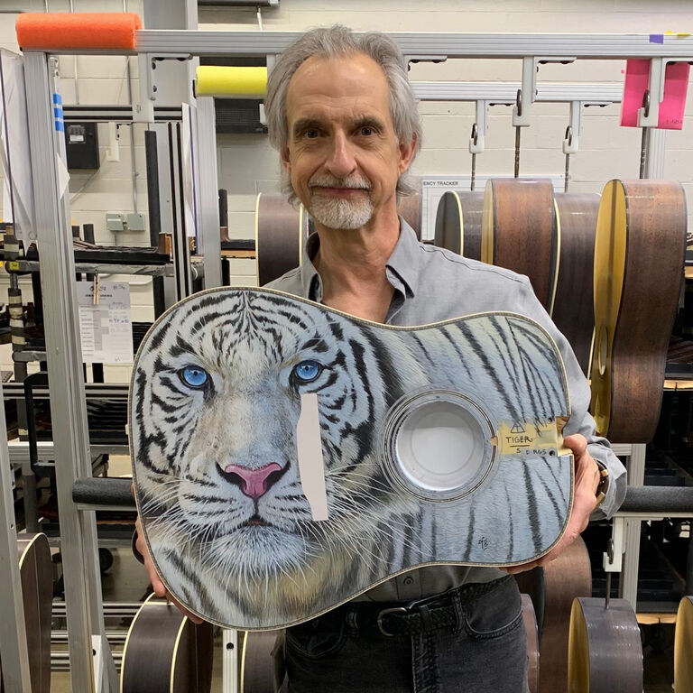 Artist Robert Goetzl holding the body of an acoustic guitar with a white tiger painted on it