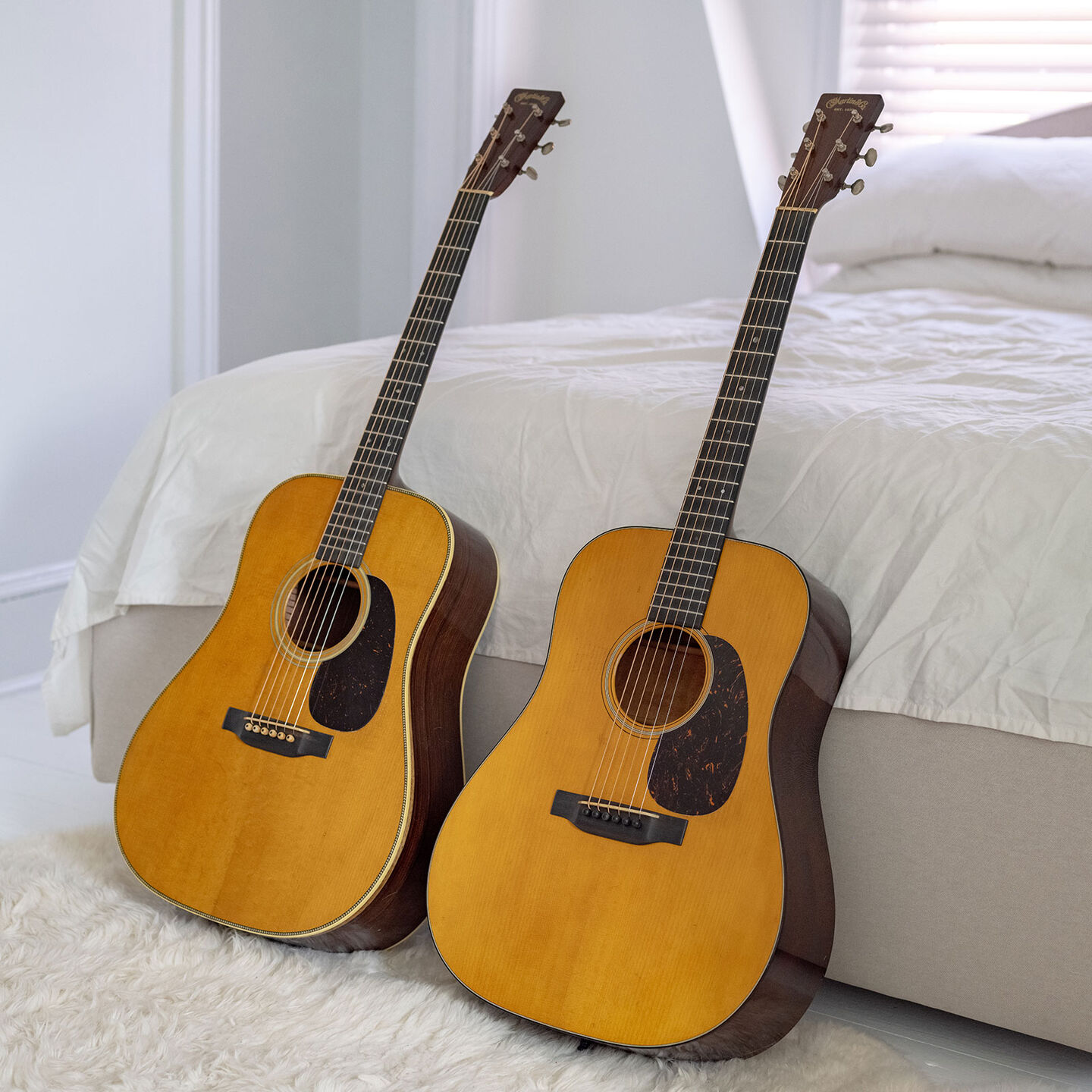 Two acoustic guitars sitting upright on a white floor