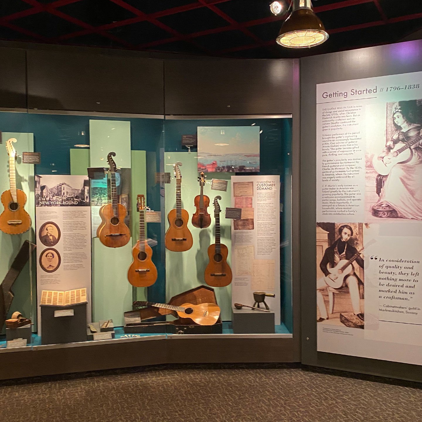 A display case in the martin museum featuring multiple acoustic guitars with posters explaining their history