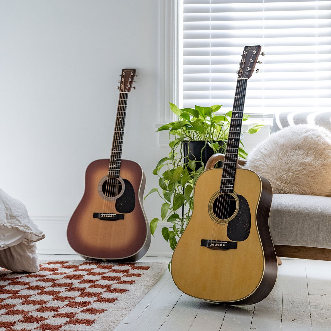 Two acoustic guitars sitting upright on a white floor