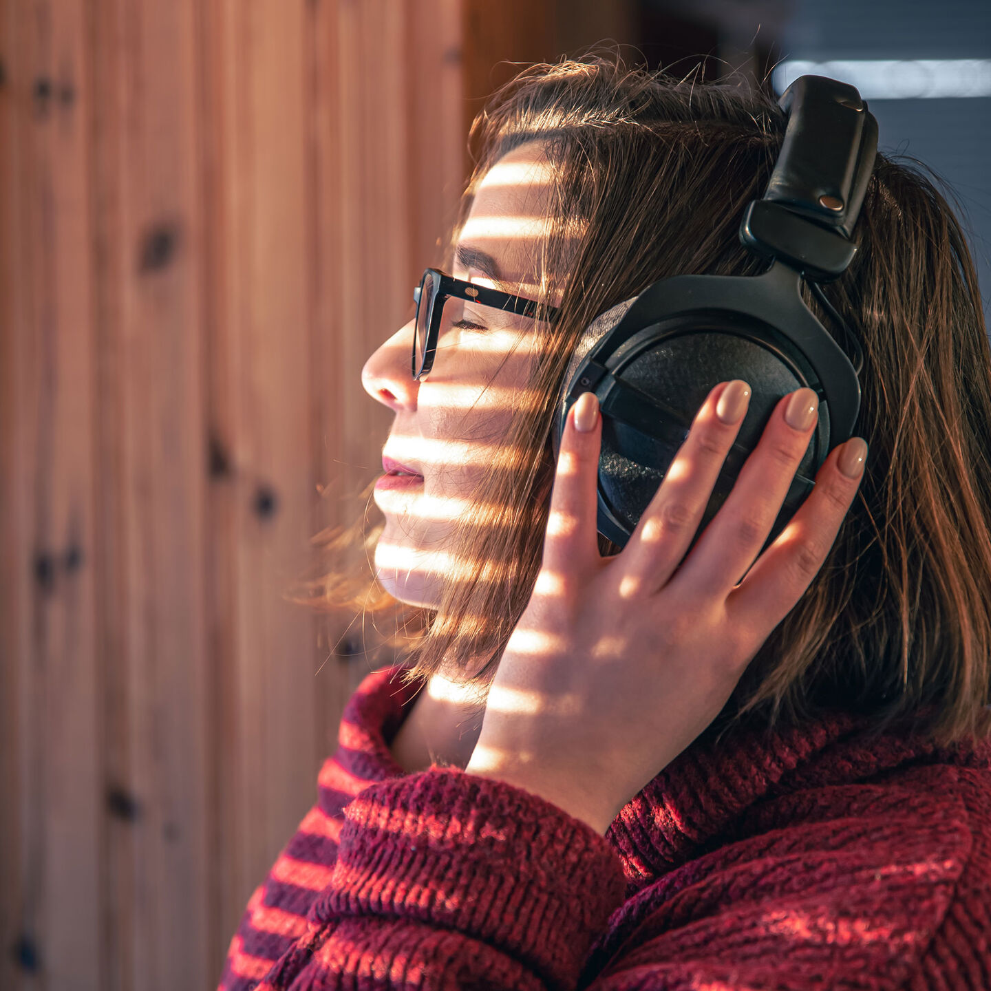 A woman in a red sweater wearing black headphones. Her hand are on the headphones.