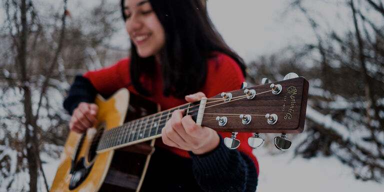 A woman in a red shirt playing a Martin guitar outside in the snow