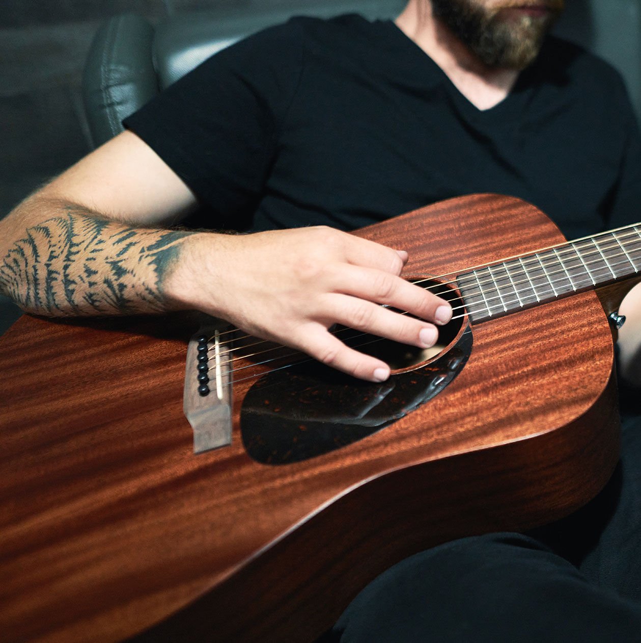 Man with tattoos playing an acoustic guitar