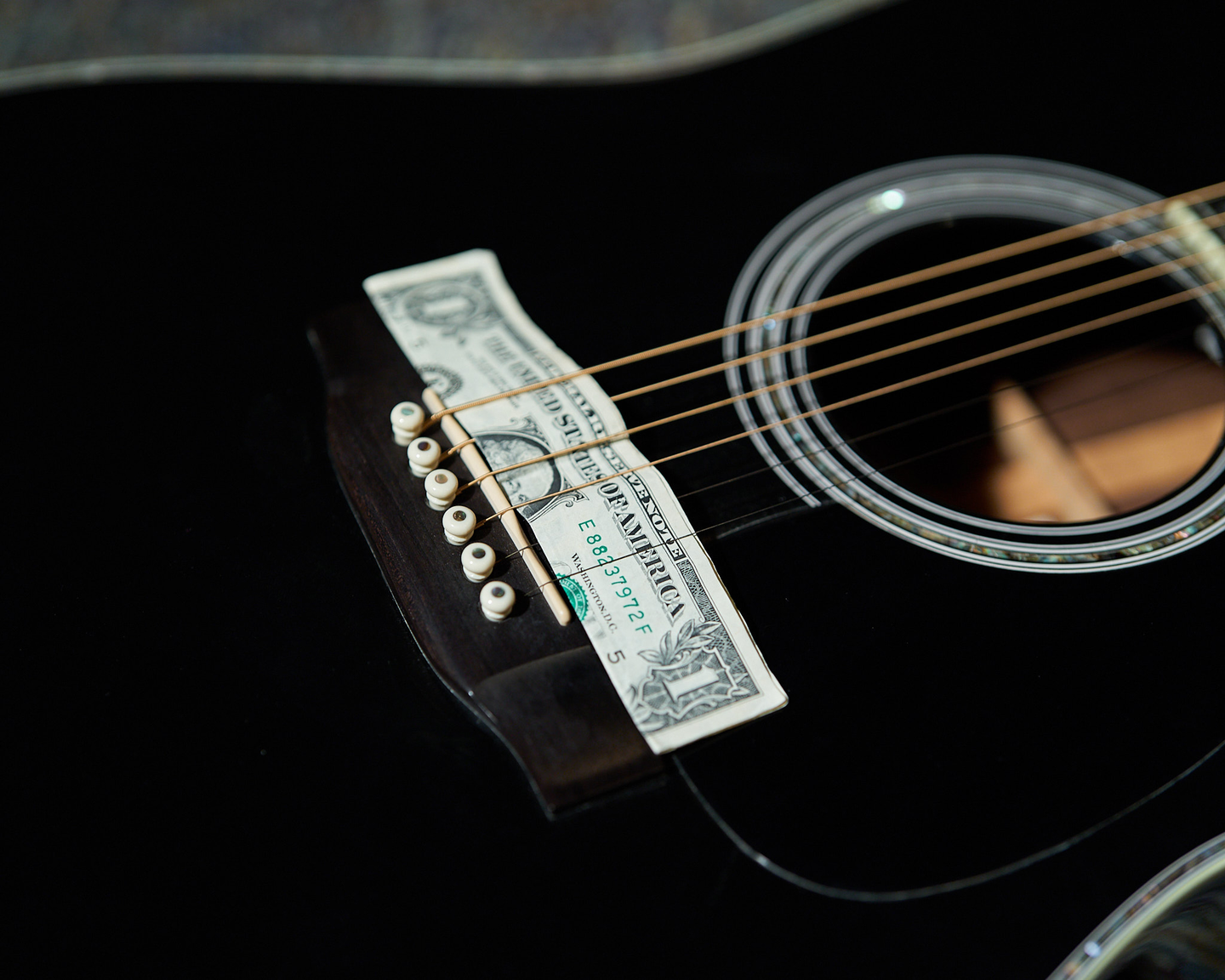 Photo of a dollar bill on the bridge of a black guitar