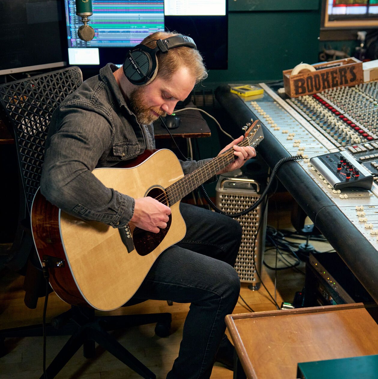 A man sitting down in a studio playing a Road Series acoustic guitar
