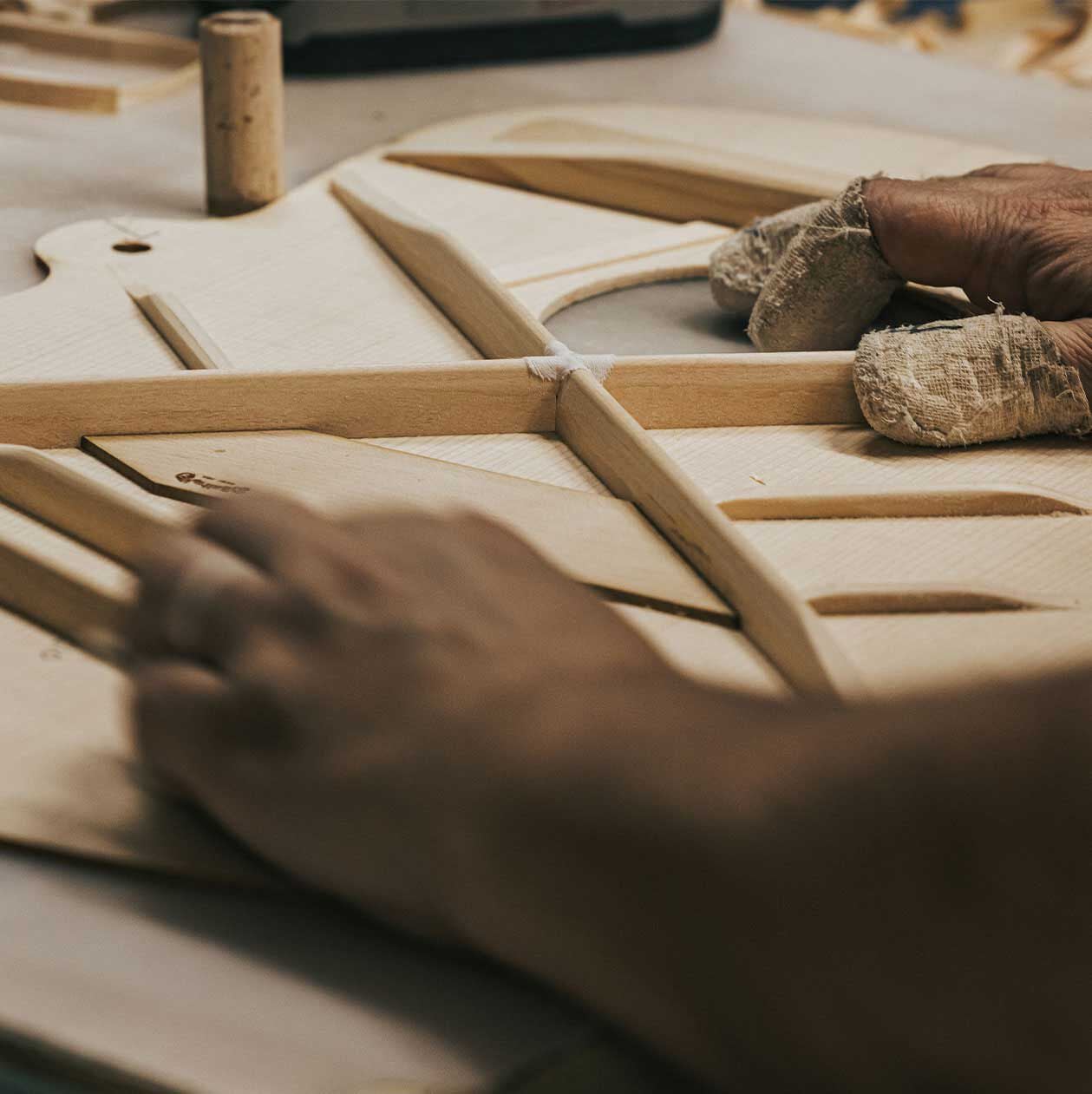 Close up photo of hands setting bracing on an acoustic guitar top