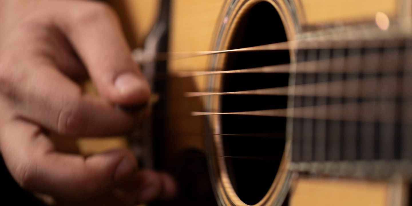 Closeup of a person strumming acoustic guitar strings