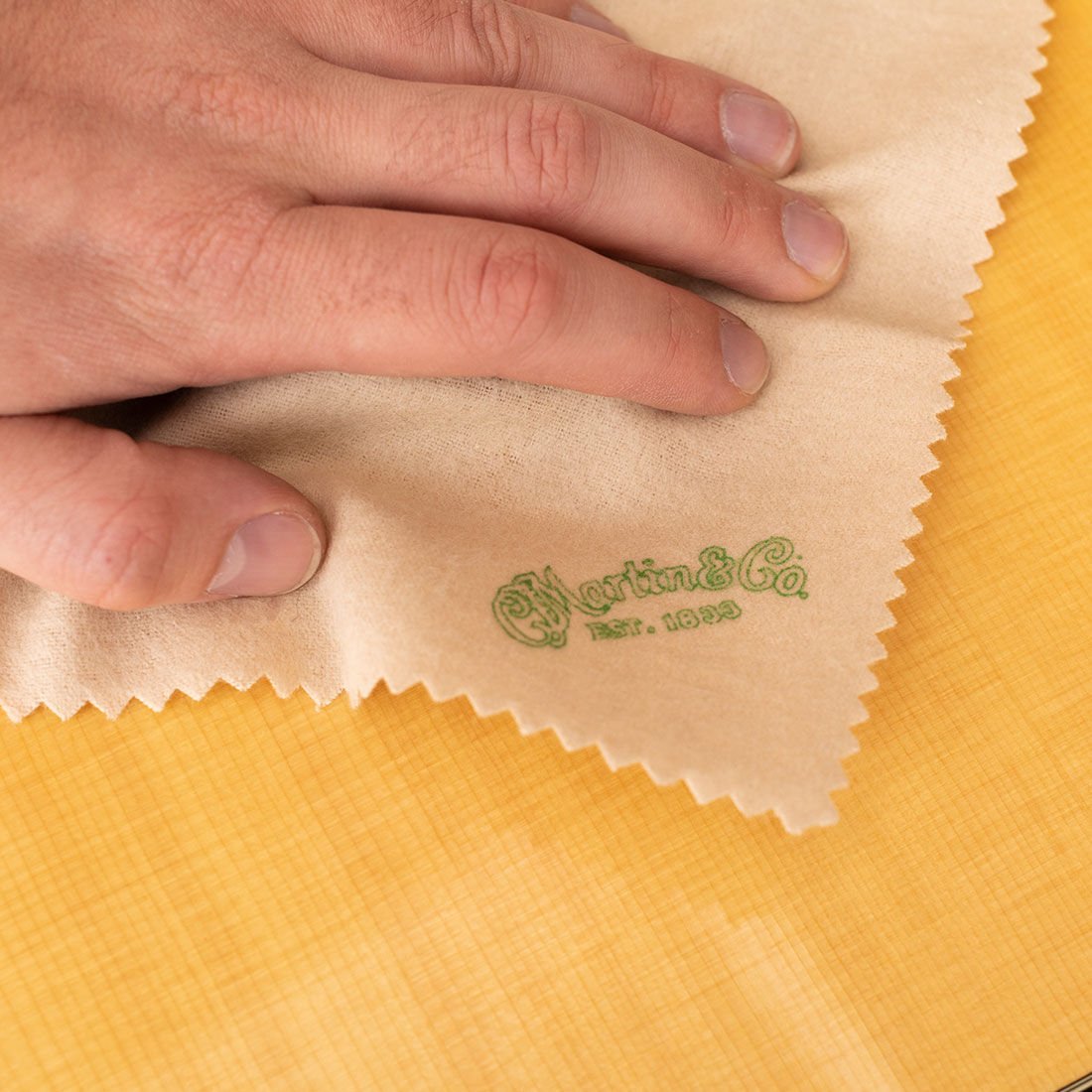 Person wiping off their acoustic guitar with a Martin-branded microfiber cloth Person wiping off their acoustic guitar with a Martin-branded microfiber cloth