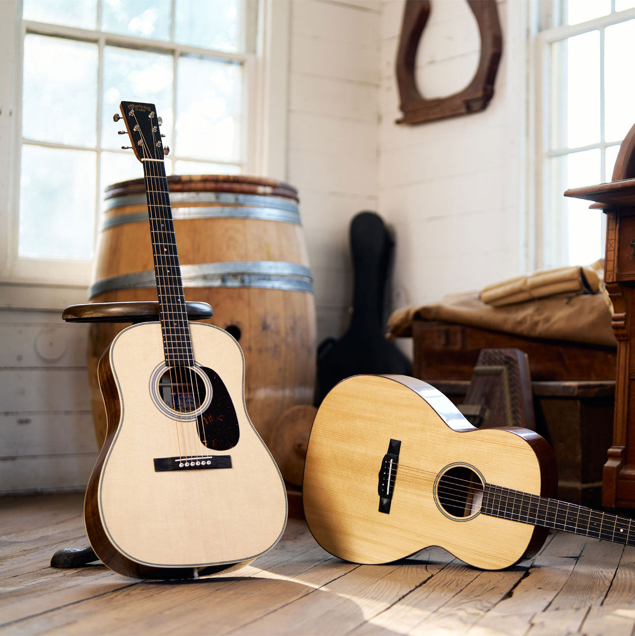 Two guitars, one standing up, one layind down on hardwood floor.