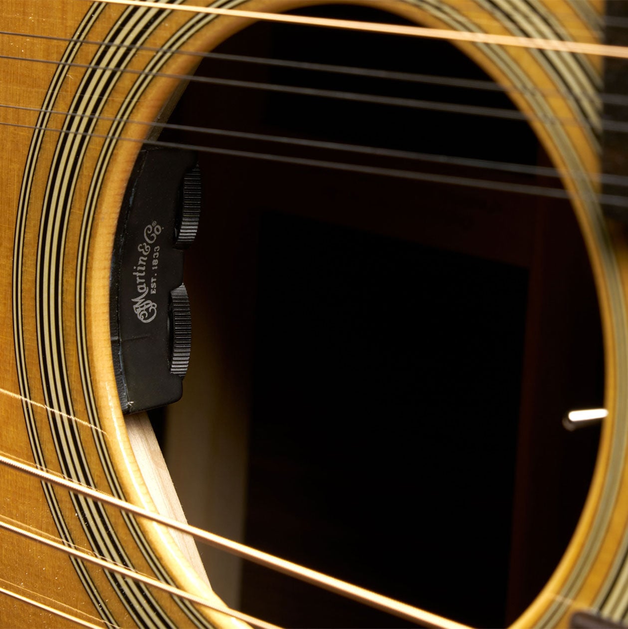 Closeup shot of the sound hole, with the two separate sets of strings crossing the body of the Grand J-28E DN