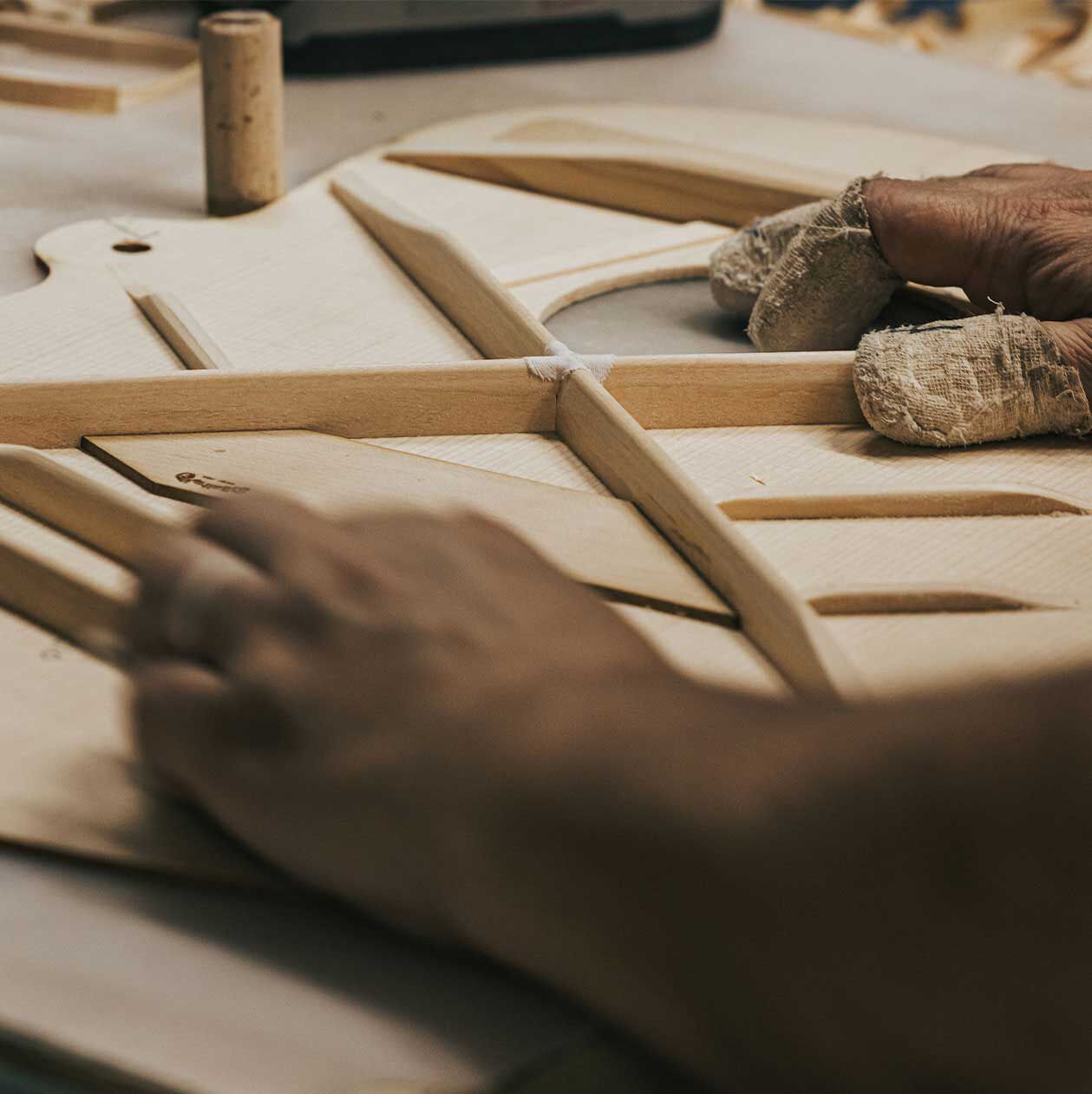 Close up photo of hands setting bracing on an acoustic guitar top
